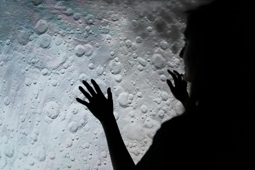 A mysterious silhouette of a woman interacting with a moon surface projection, evoking exploration and wonder.